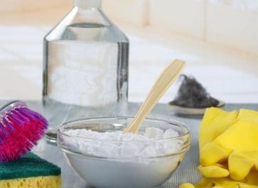 baking soda in glass bowl with a jar of vinegar behind it and cleaning gloves