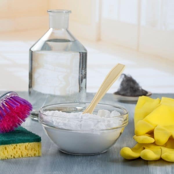 baking soda in glass bowl with a jar of vinegar behind it and cleaning gloves