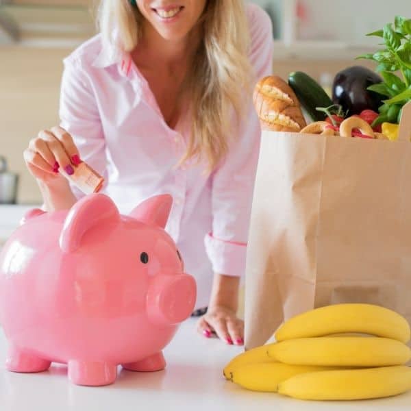 5 tips to slash your grocery budget as woman puts savings in pink pig piggy bank