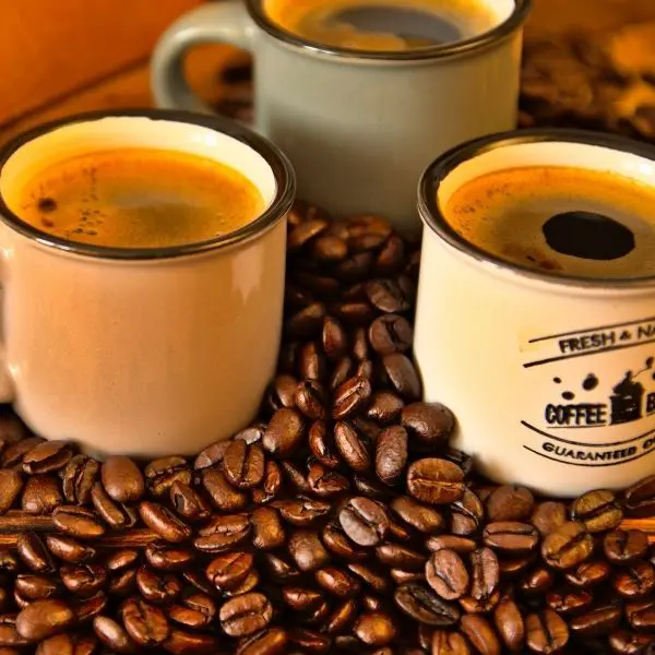 coffee cups filled with coffee sitting on top of whole coffee beans