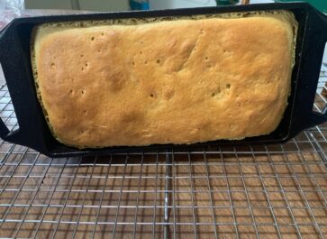 loaf of einkorn bread in a cast iron baking pan cooling on a wire rack