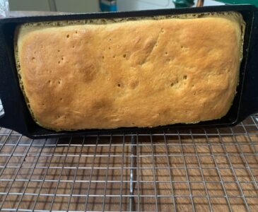 loaf of einkorn bread in a cast iron baking pan cooling on a wire rack