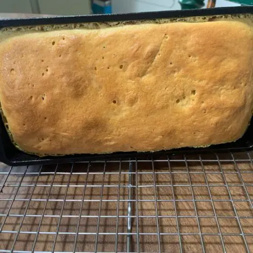 loaf of einkorn bread in a cast iron baking pan cooling on a wire rack