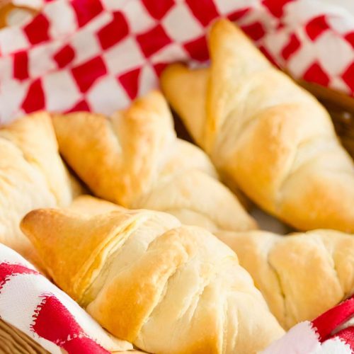 homemade einkorn crescent rolls in a basket lined with red and white checkered fabric