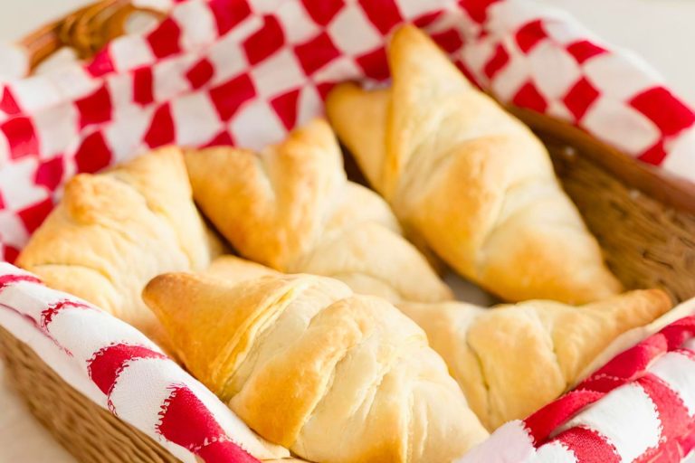 homemade einkorn crescent rolls in a basket lined with red and white checkered fabric