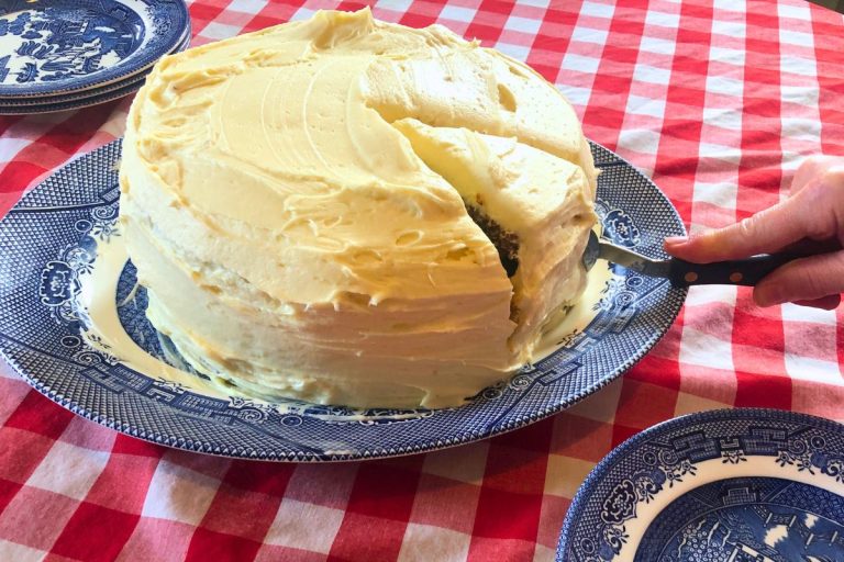 einkorn carrot cake with cream cheese frosting on a blue willow platter on a red and white checkered tablecloth