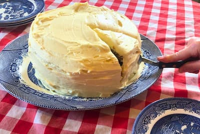einkorn carrot cake with cream cheese frosting on a blue willow platter on a red and white checkered tablecloth