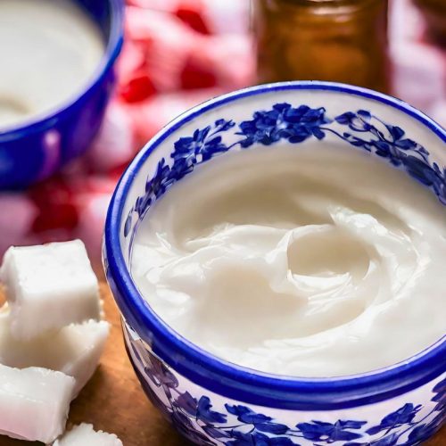 coconut oil in a blue and white bowl on a wooden cutting board on a red and white checkered tablecloth