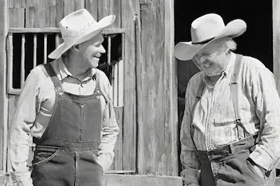 black and white photo of two old farmers standing in front of a barn and laughing