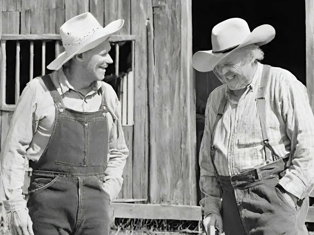 black and white photo of two old farmers laughing while standing in front of a barn as they talk about old sayings and their meanings