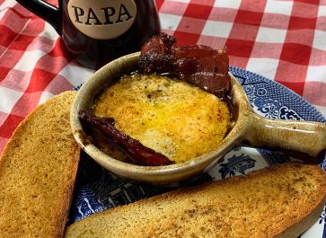 blue willow plate with a brown ceramic bowl with egg bowl recipe cooked in it with bacon and toast