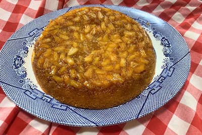 from scratch pineapple upside down cake with chunk pineapples on a blue willow plate sitting on a red gingham table cloth
