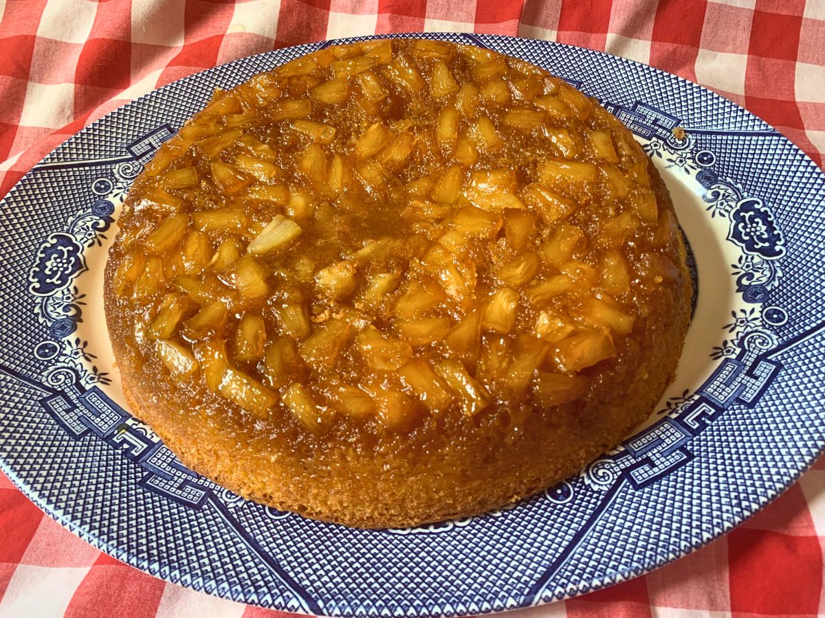 from scratch pineapple upside down cake with chunk pineapples on a blue willow plate sitting on a red gingham table cloth