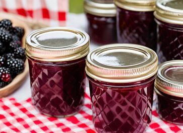 blackberry jam in canning jars sitting on a red gingham tablecloth