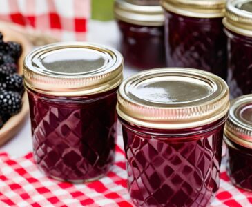 blackberry jam in canning jars sitting on a red gingham tablecloth