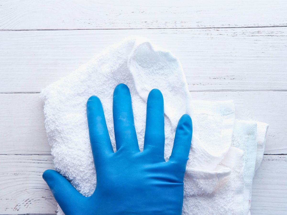 womans and wearing a blue cleaning glove using a white rag and salt to clean a table that is painted white to show how to use salt as a disinfectant