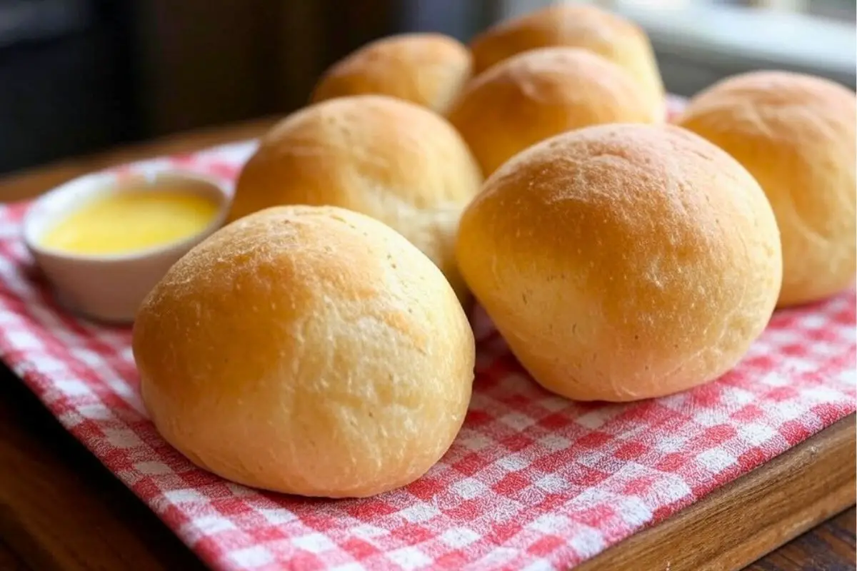 einkorn dinner rolls on a wooden cutting board covered with a red gingham cloth and a bowl of melted butter on the side