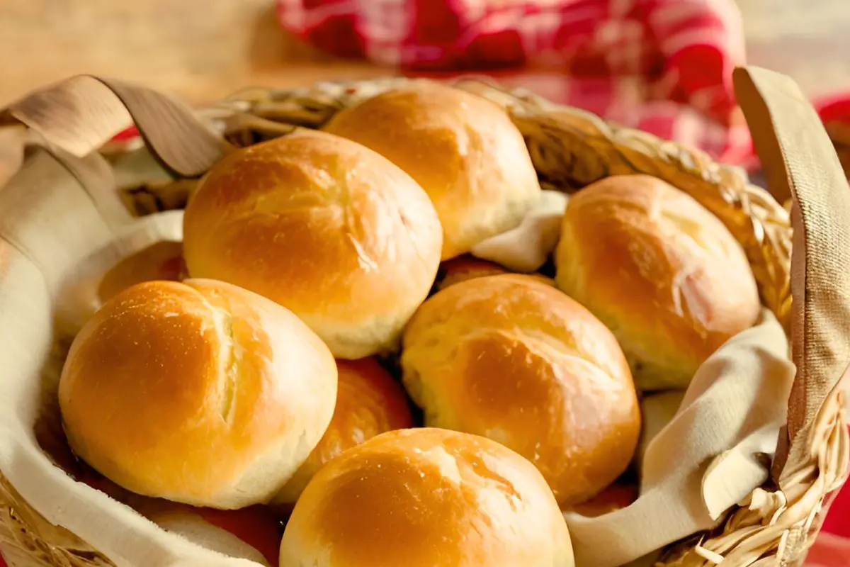 a woven basket of baked einkorn dinner rolls with red gingham cloth