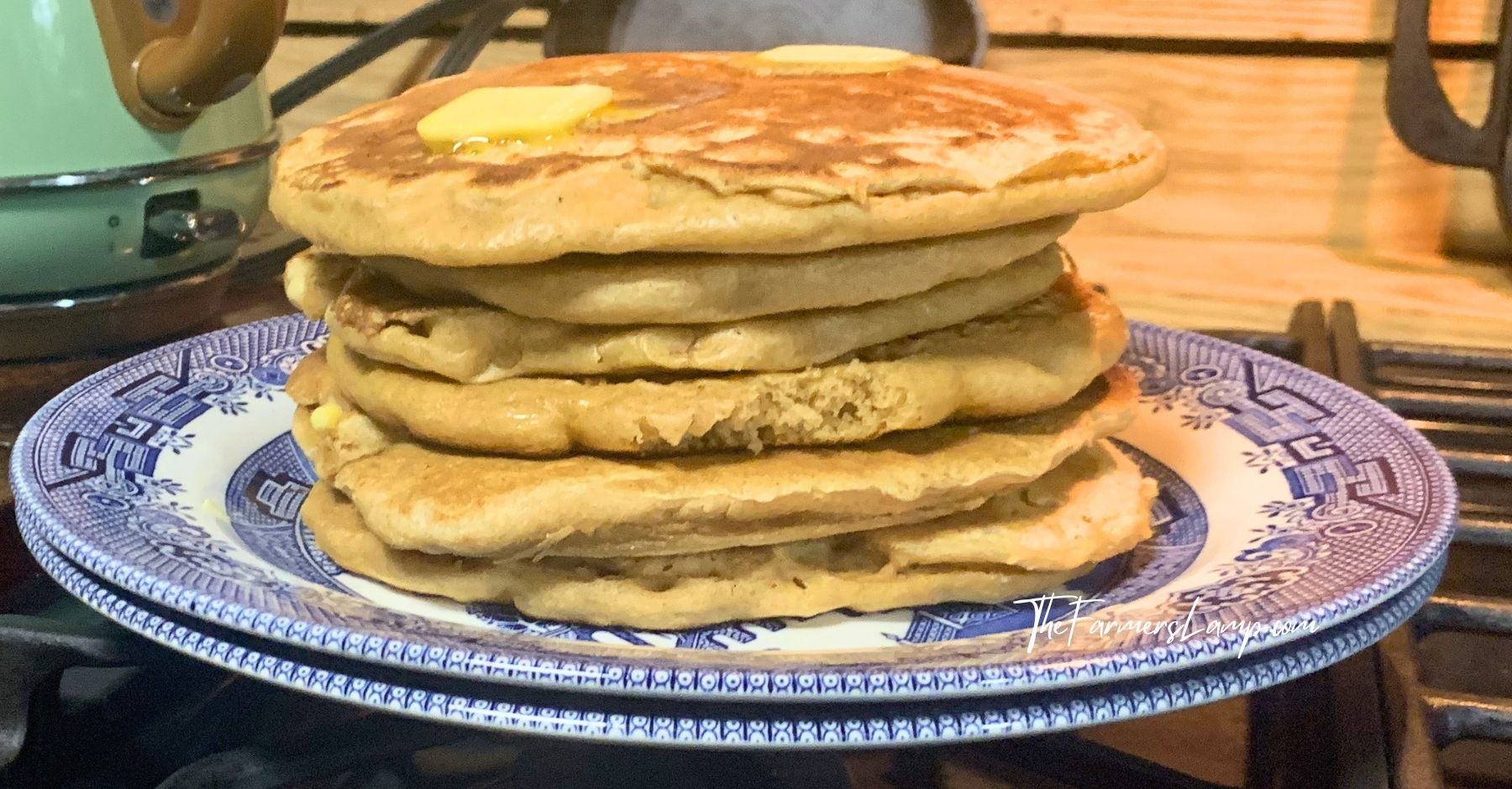 spelt flour pancakes stacked on a blue willow plate with butter on them