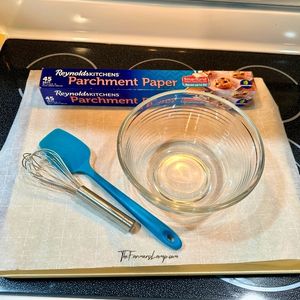 Parchment paper in a box, glass bowl, whisk, and spatula for use in this recipe.